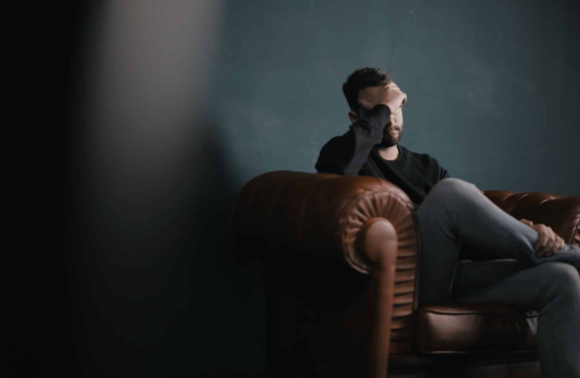 man depressed with sitting in chair with hand on forehead