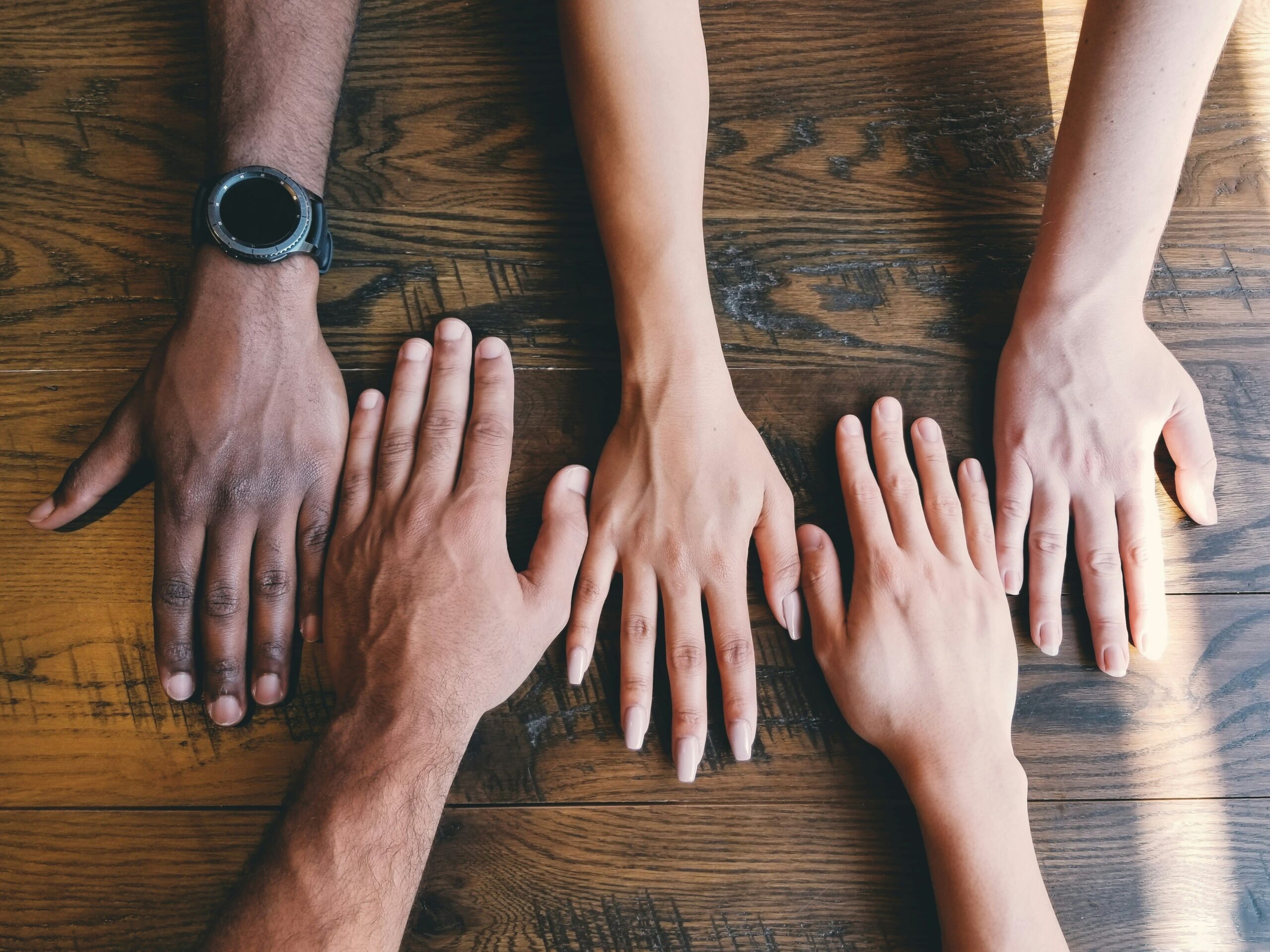 an image of peoples hands reaching over the end of the table showing diversity.